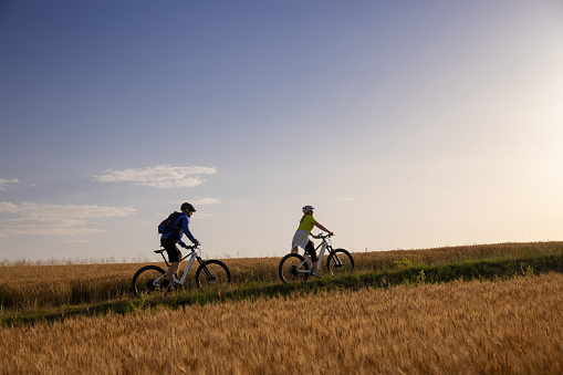 Couple riding bicycle uphill on rural field against sky