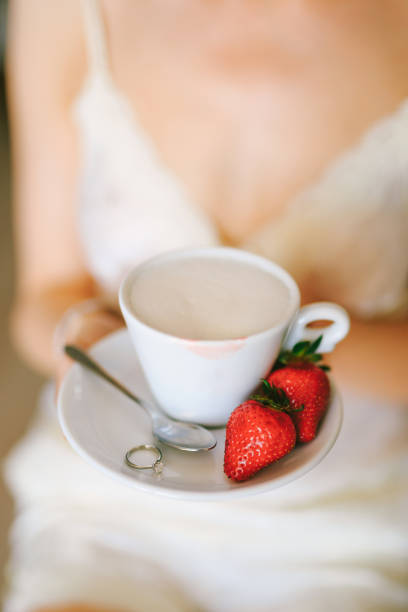 uma garota de vestido branco segura em suas mãos um pires com uma xícara de cappuccino, dois morangos, uma colher de chá e um anel. close-up - coffee hot drink cup teaspoon - fotografias e filmes do acervo
