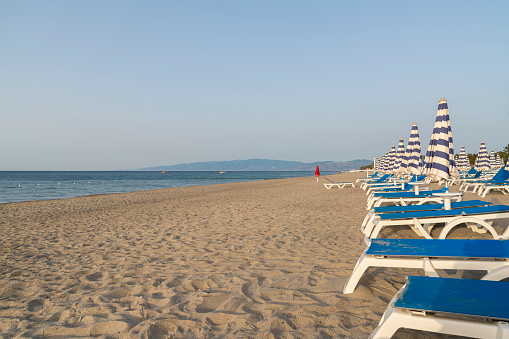 Blue and white umbrella and beach chairs at the beach in front of blue sea and blue sky. Calabria, Simeri Mare, Italy.