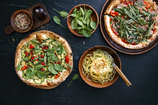 Italian steak pizza with tomato, arugula, microgreen and pesto sauce. Pizza with zucchini, sun-dried tomatoes pesto sauce, spinach, seeds and nuts. Vegetarian spaghetti with zucchini, arugula, seeds, vegan cheese and pesto sauce. Flat lay top-down composition on dark background.