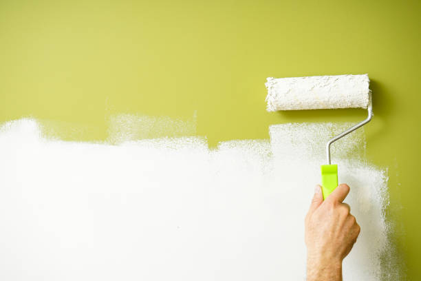istock Paint roller in the hand of a man repainting the wall, space for text. 1353436090