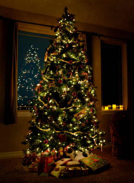 istock Christmas tree with lights and presents inside a home with big windows at night in the dark 1353436233
