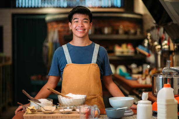 asiatico cinese sorridente adolescente ragazzo panettiere che guarda la macchina fotografica in cucina - asian country foto e immagini stock