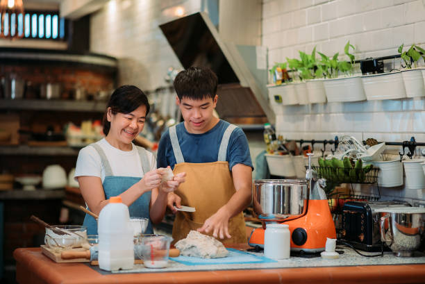 Asian chinese smiling baker mother and son preparing dough togethers in the kitchen stock photo