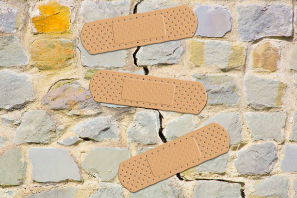 Old cracked and damaged stone wall cause due to subsidence of foundations structural failures - concept with adhesive bandage Old cracked and damaged stone wall cause due to subsidence of foundations structural failures - concept with adhesive bandage crevice photos stock pictures, royalty-free photos & images