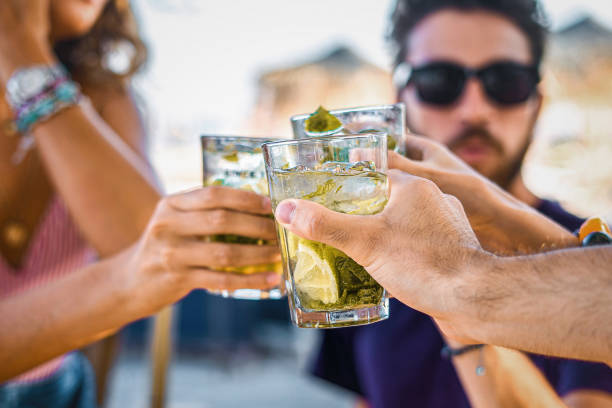 fiesta de brindis - primer plano en la mano de los jóvenes tintineando copas de cócteles celebrando la amistad juntos en el café de la playa. - gin fotografías e imágenes de stock