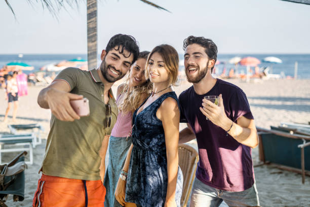 istock Young people get together taking selfie on the beach. Friends using smartphone and have fun together with the sea in the background 1353441483