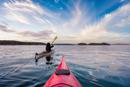 Adventurous Woman on Sea Kayak paddling in the Pacific Ocean. Dramatic Sunset Sky Art Render. Taken near Victoria, Vancouver Islands, British Columbia, Canada. Concept: Sport, Adventure