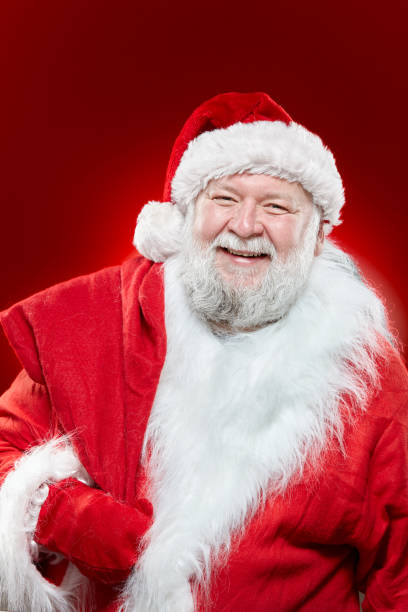 istock Happy laughing Santa Claus dressed in a red coat and a hat, keep a bag on his back, looking at camera, isolated red background. 1353444180