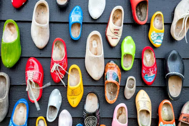 Old wooden Dutch shoes - klomps. A lot of colorful old clomps against the background of a wooden wall. Popular souvenirs. Traditions of Holland. Background