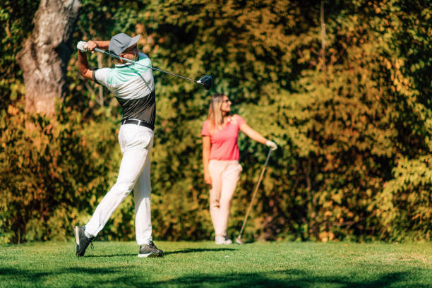 couple de golfeurs. homme en position de balançoire, dame suivant la balle en vol - golf playing teeing off men photos et images de collection