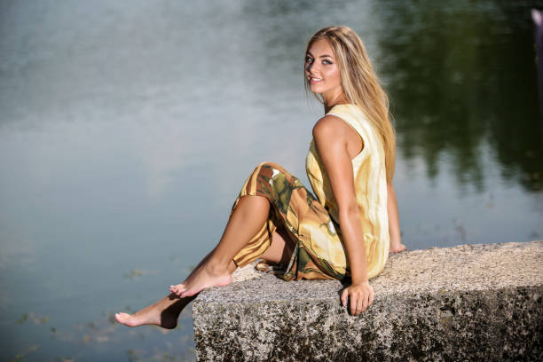Beautiful blonde in a yellow dress enjoys a sunny day by the lake