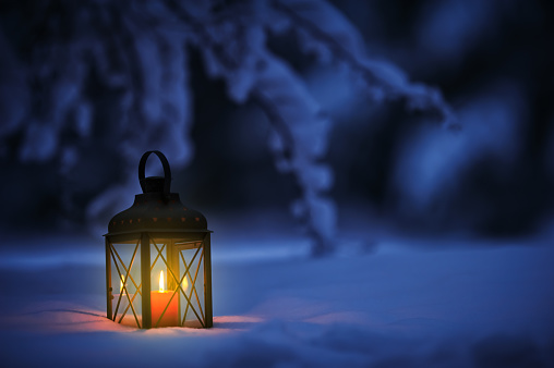 Candle lantern in snow at dusk. Christmas time in a wintery garden.