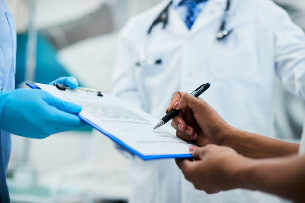 Close-up of woman signing medical agreement at doctor's office. Close-up of African American woman signing paperwork during medical appointment at clinic. health insurance stock pictures, royalty-free photos & images