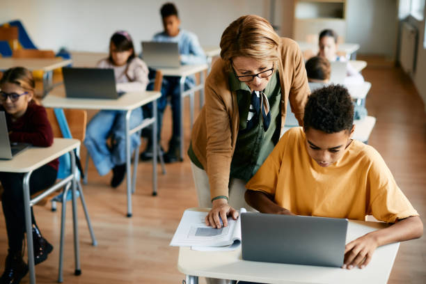 istock African American schoolboy using laptop with help of his teacher during computer class in the classroom. 1353453848