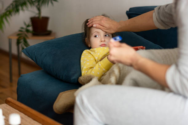 istock Girl lying on sofa while her single mother is checking her temperature 1353453961