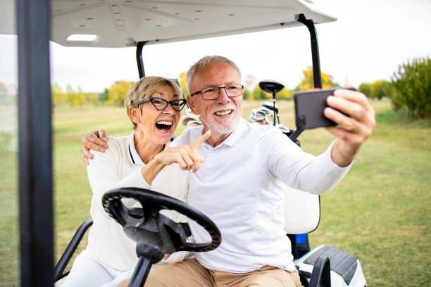 uśmiechnięta para seniorów bawiąc się na polu golfowym i robiąc sobie zdjęcie selfie w samochodzie golfowym przed treningiem. - golf green practicing sports training zdjęcia i obrazy z banku zdjęć