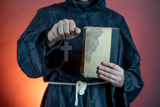 A man in a monastic cassock holds an old book and a crucifix in his hands