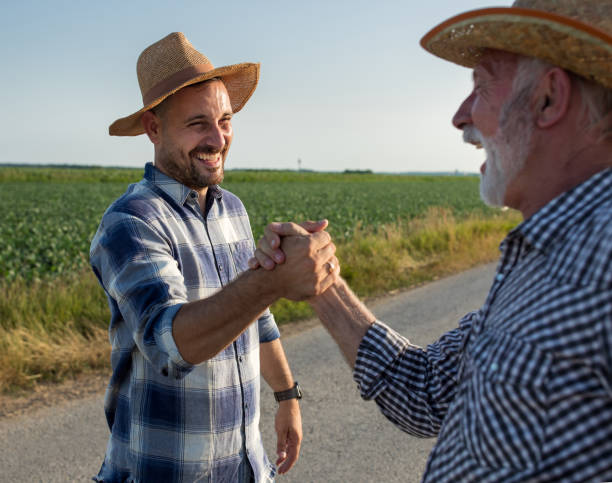 Two farmers shaking hands as greeting in field stock photo