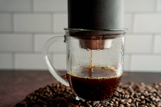 istock Transparent glass coffee cup under a pour over coffee maker as fresh coffee drips into cup on a pile of fresh roasted whole bean coffee 1353458531