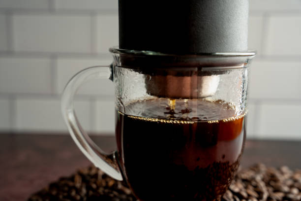 istock Transparent glass coffee cup under a pour over coffee maker as fresh coffee drips into cup on a pile of fresh roasted whole bean coffee 1353458534