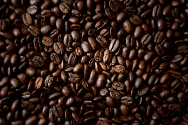 chicchi di caffè appena tostati in una pila su uno sfondo rustico - chicco di caffè foto e immagini stock
