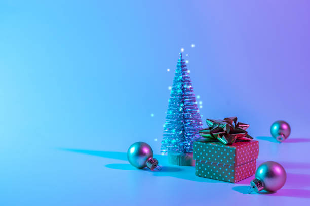 istock Neon Christmas winter background. Minimal abstract tree, xmas gift box. Holiday decoration bauble ball on neon gradient backdrop. Happy new year copy space. 1353459282