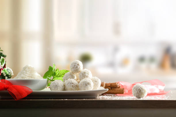 Kitchen table with coconut balls prepared for event with bowl with grated coconut and white kitchen background Front view. Horizontal composition.