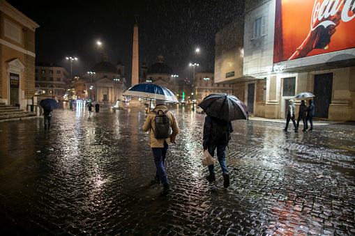 Rome, Italy - November 06, 2021: People in the city cross the street protecting themselves from the rain with umbrellas. Citizens in the rain.