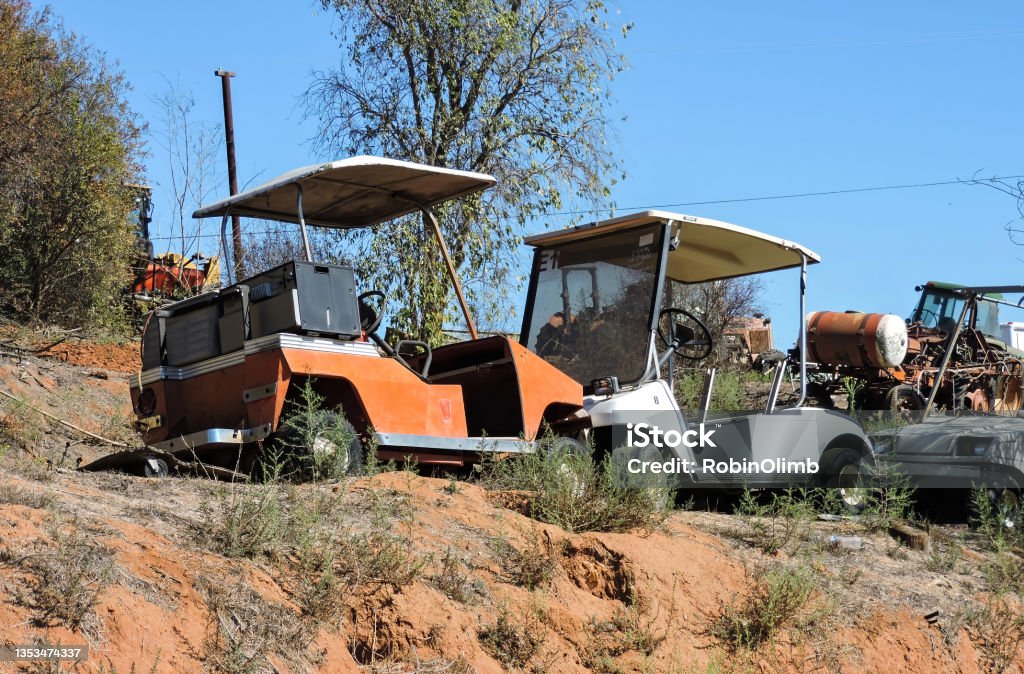 Old Weathered Golf Carts Two vintage weathered golfs on a dirt ridge with weeds around them. Cart Stock Photo