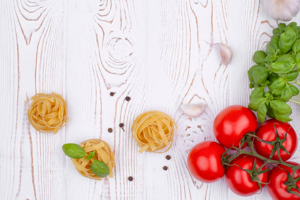 istock Top view raw tagliatelle pasta with fresh basil, garlic and tomatoes on a rustic white table, flat lay, copy space. 1353474659