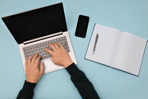 istock Top view of man hands typing on laptop keyboard in the office with mobile phone, open empty notebook and pencil on the side. 1353476702
