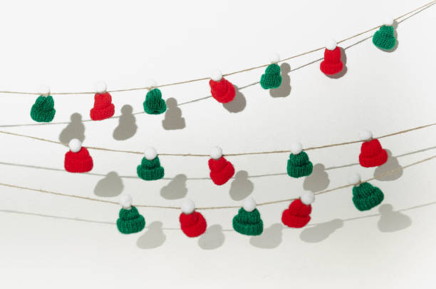 istock Green and red caps with white pompoms hanging on ropes. White background. 1353477314