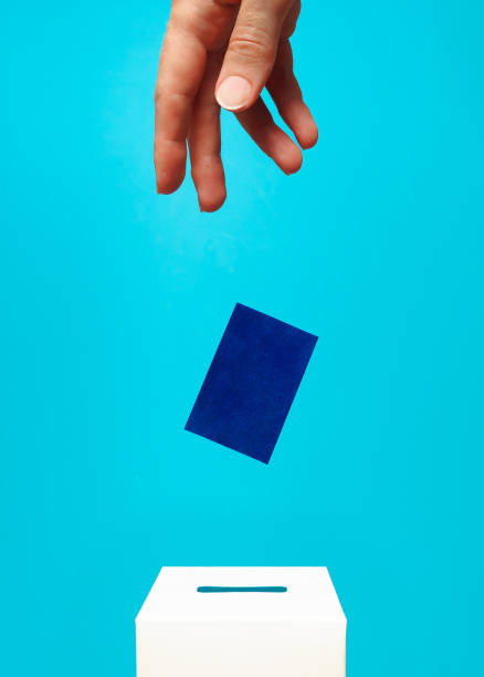 istock election concept - a woman's hand puts a blue card into a white voting box 1353482230