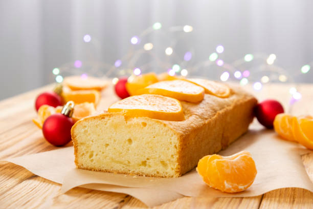 barra de tarta de mandarina sin gluten con trozos de mandarina, juguetes navideños y luces sobre fondo rústico de madera. tarta de cítricos por receta clásica para las vacaciones de invierno. - pound cake fruitcake cake loaf of bread fotografías e imágenes de stock