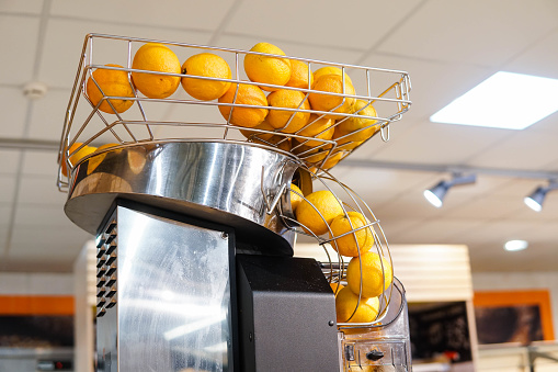 Fresh orange fruits in orange juice machine at store. Juicer in the supermarket.