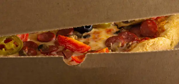 Photo of Tasty pizza in box. Peep into the narrow gap.