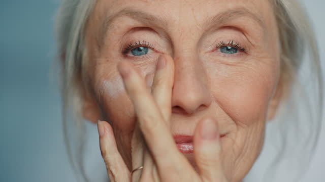 Portrait of Beautiful Senior Woman Gently Applying Under Eye Face Cream. Elderly Lady Makes Her Skin Soft, Smooth, Wrinkle Free with Natural anti-aging Cosmetics. Product for Beauty Skincare, Makeup