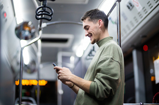 Men  using her mobile phone outdoors at night. Young man in public bus using phone and texting online