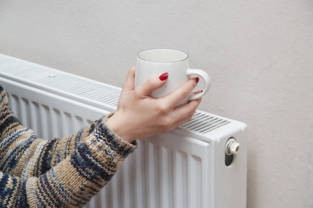 istock Woman warming hands with tea cup and heating radiator. 1353495136
