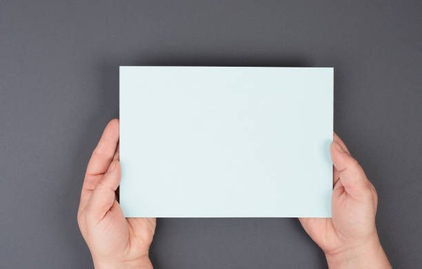 istock Woman holds a blank sheet of paper, gray colored background, empty copy space for text, minimalism 1353495285