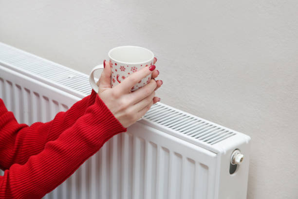 istock Woman warming hands with tea cup and heating radiator. 1353495643