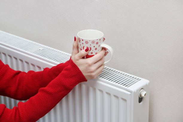 istock Woman warming hands with tea cup and heating radiator. 1353495644