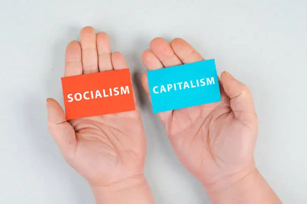 Photo of The words socialism and capitalism are standing on piece of papers, hands holding the message, political issue