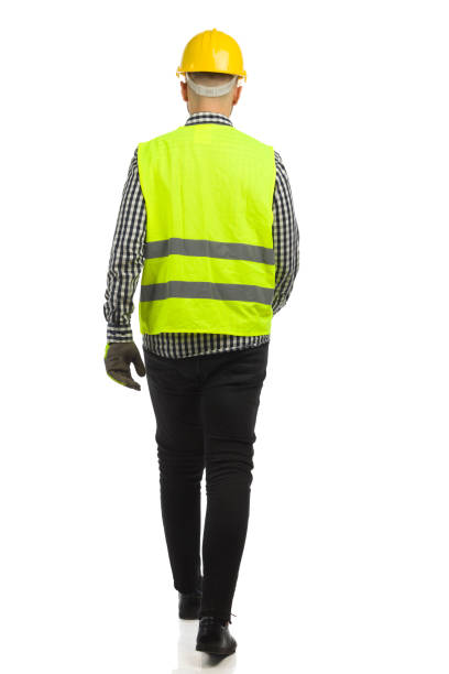 istock Walking man in hardhat and reflective vest. Rear view. Full length on white background. 1353504520