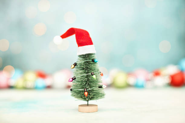 istock Christmas Background with Tiny Christmas Tree Decorated in String Lights and a Santa Hat 1353527575