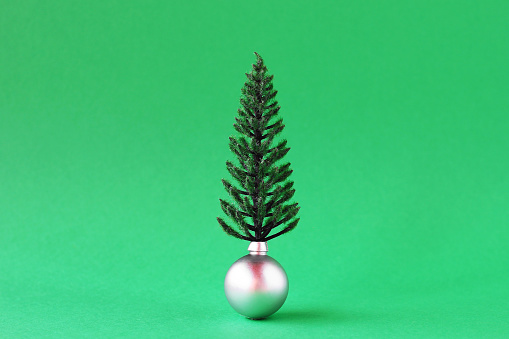 Christmas decorations - shiny silver ball artificial Christmas tree on green background with copy space. Minimal Christmas and New Year concept.