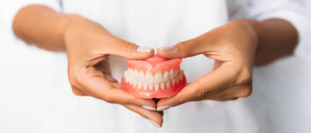 The dentist is holding dentures in his hands. Dental prosthesis in the hands of the doctor close-up. Front view of complete denture. Dentistry conceptual photo. Prosthetic dentistry. False teeth stock photo