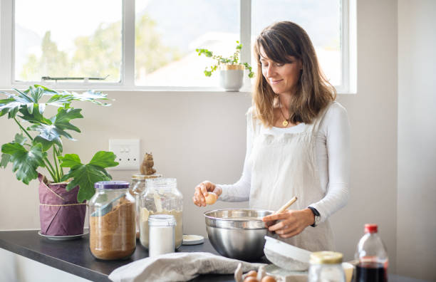 istock Smiling young woman cracking an egg into a mixing bowl in her kitchen 1353551578