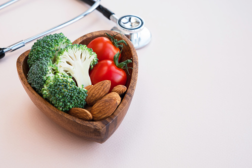 Plate with vegetables, nuts and a medical stethoscope on the table. Diet and medicine concept. Close up, copy space
